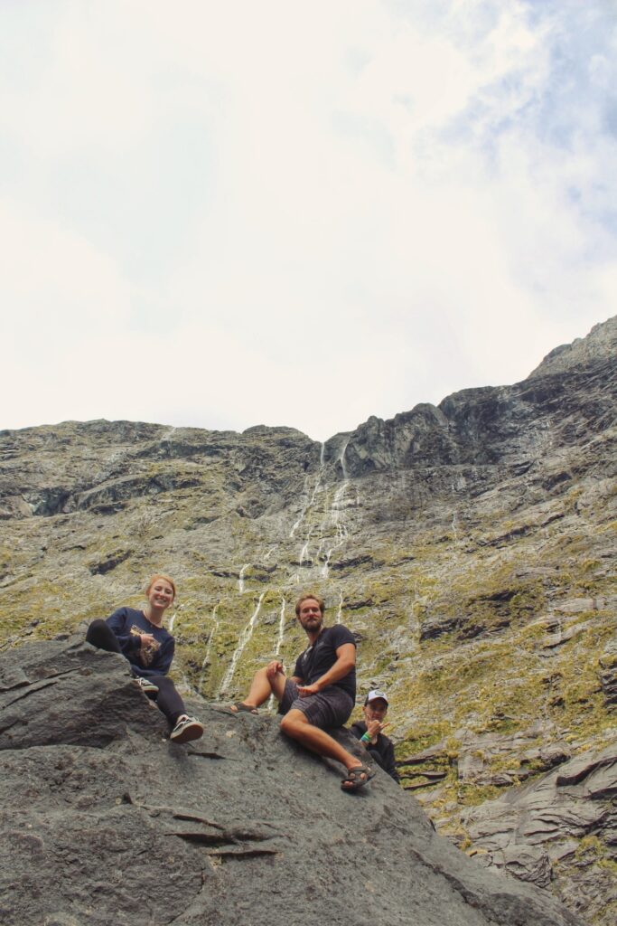 thousand waterfalls, milford sound, new zeaalnd. people sitting on large rock in foreground