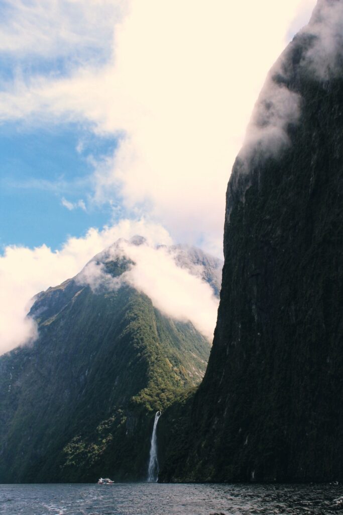milford sound, new zealand. vast cliffs with waterfalls and boat in the distance