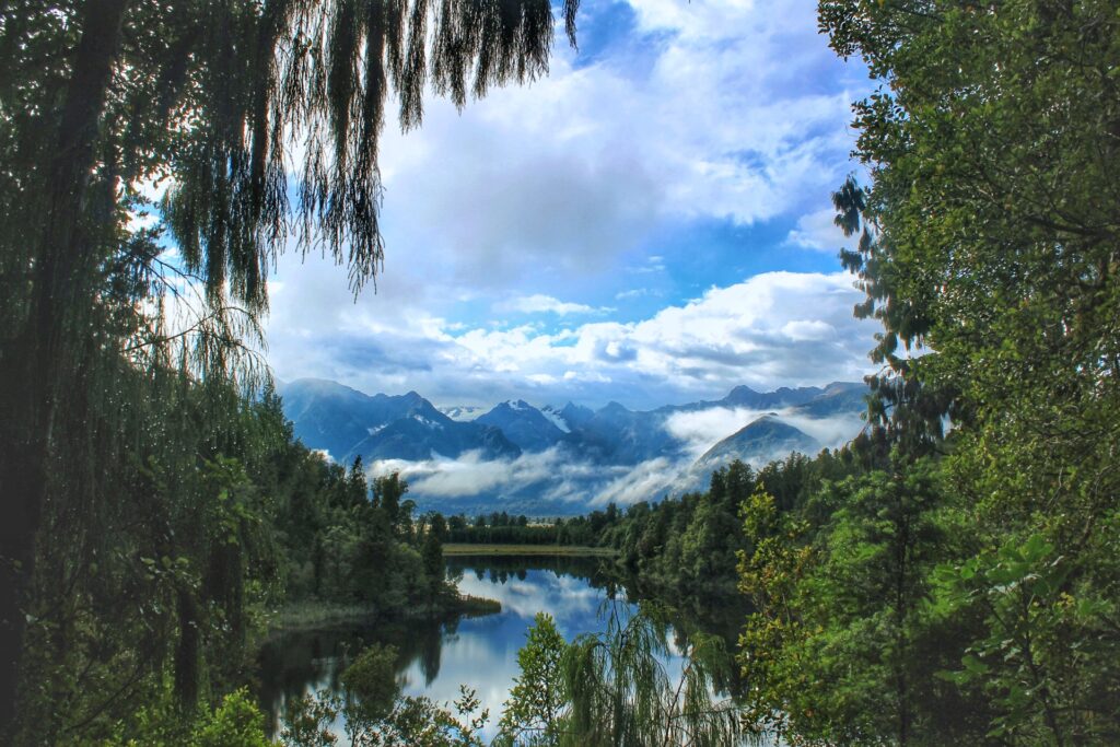 Lake Matheson, New Zealand, framed by trees with a reflective lake and mountains in the background
