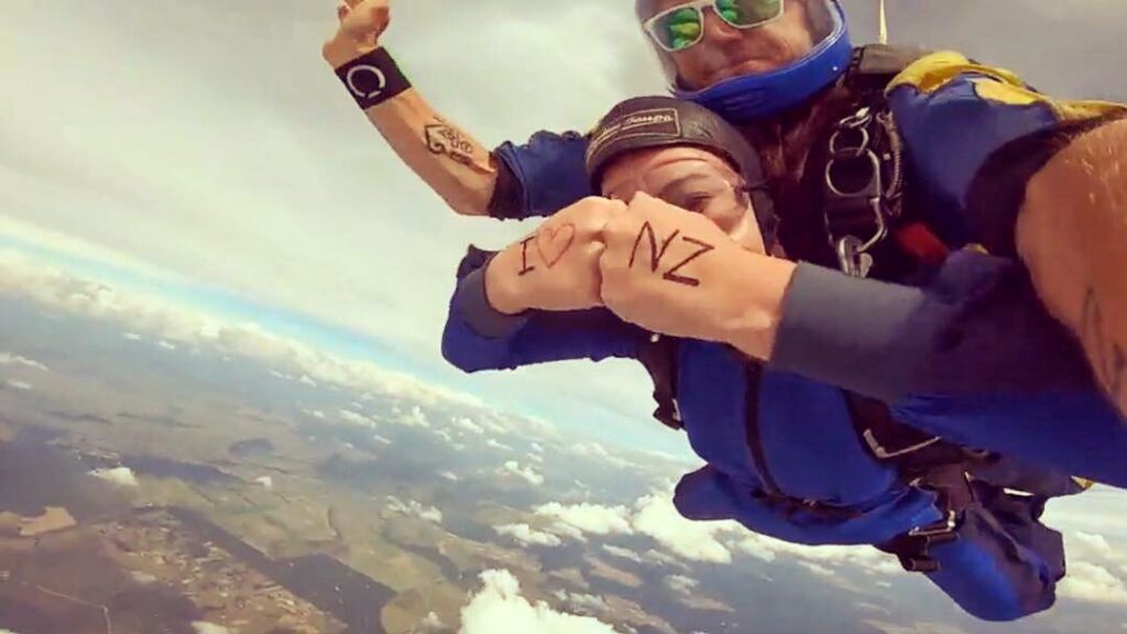 melody skydiving in taupo, new zealand. holding fists infront of her with writing I LOVE NZ
