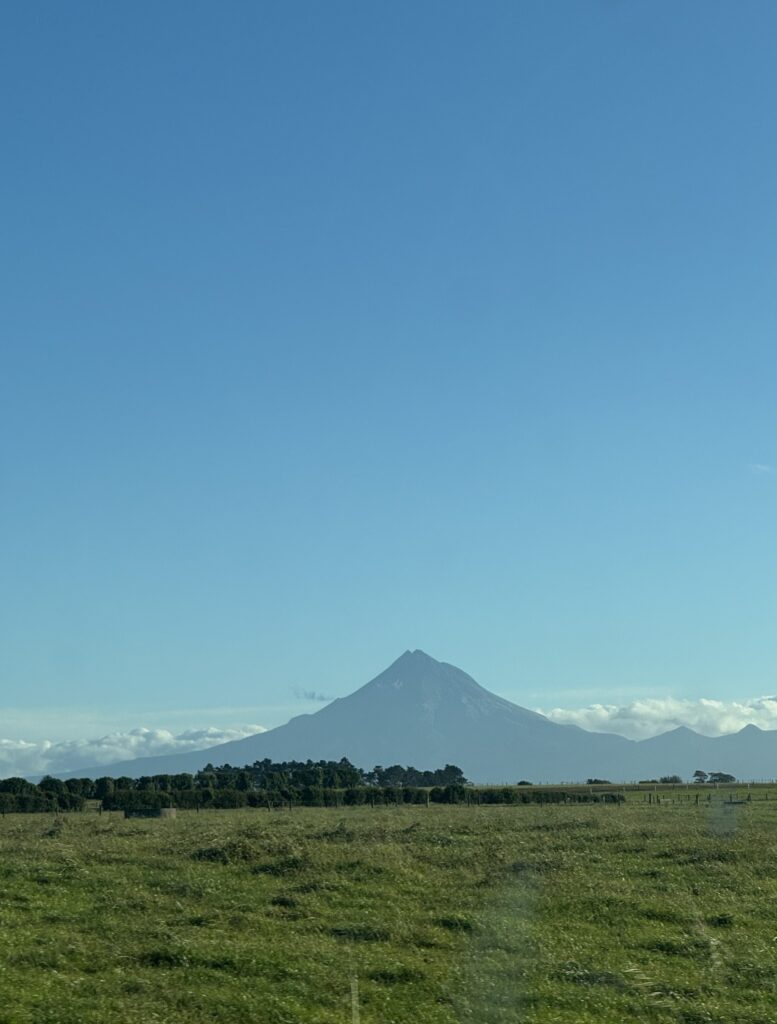 mount taranaki, new zealand. photo taken from far away. green field in foreground