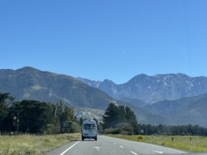 campervan driving through south island of new zealand. fields on either side and snow capped mountains in background