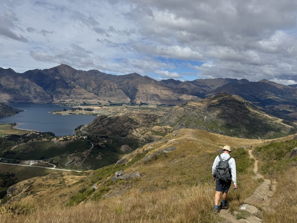 mountain view from rocky mountain summit hike, new zealand. man walking down hill in foreground