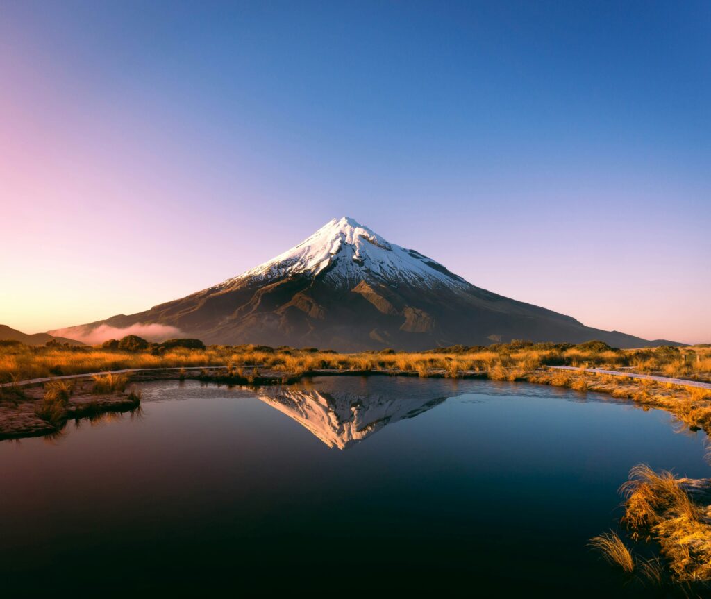 snow capped mount taranaki, new zealand taken from Pouākai tarn. lake reflecting volcano.