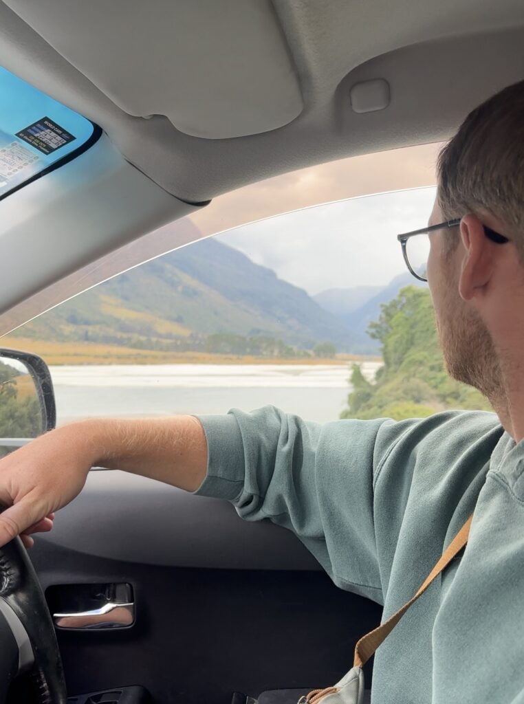 man driving car in queenstown, new zealand