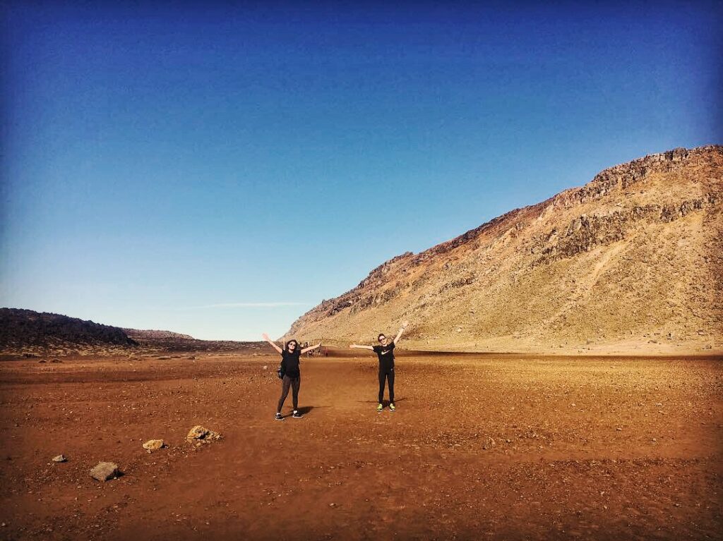 melody and friend hiking tongariro crossing new zealand. standing on red sand with rocks in background.