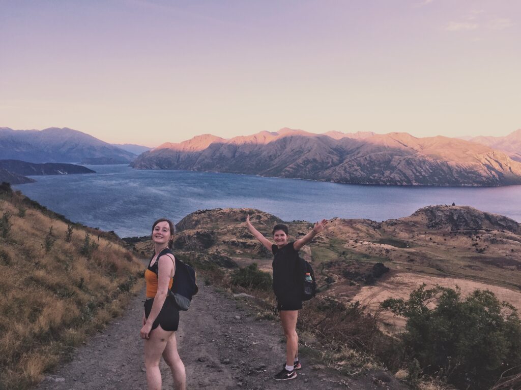 view coming down from roys peak, wanaka, new zealand. melodys friends standing with arms outstretched
