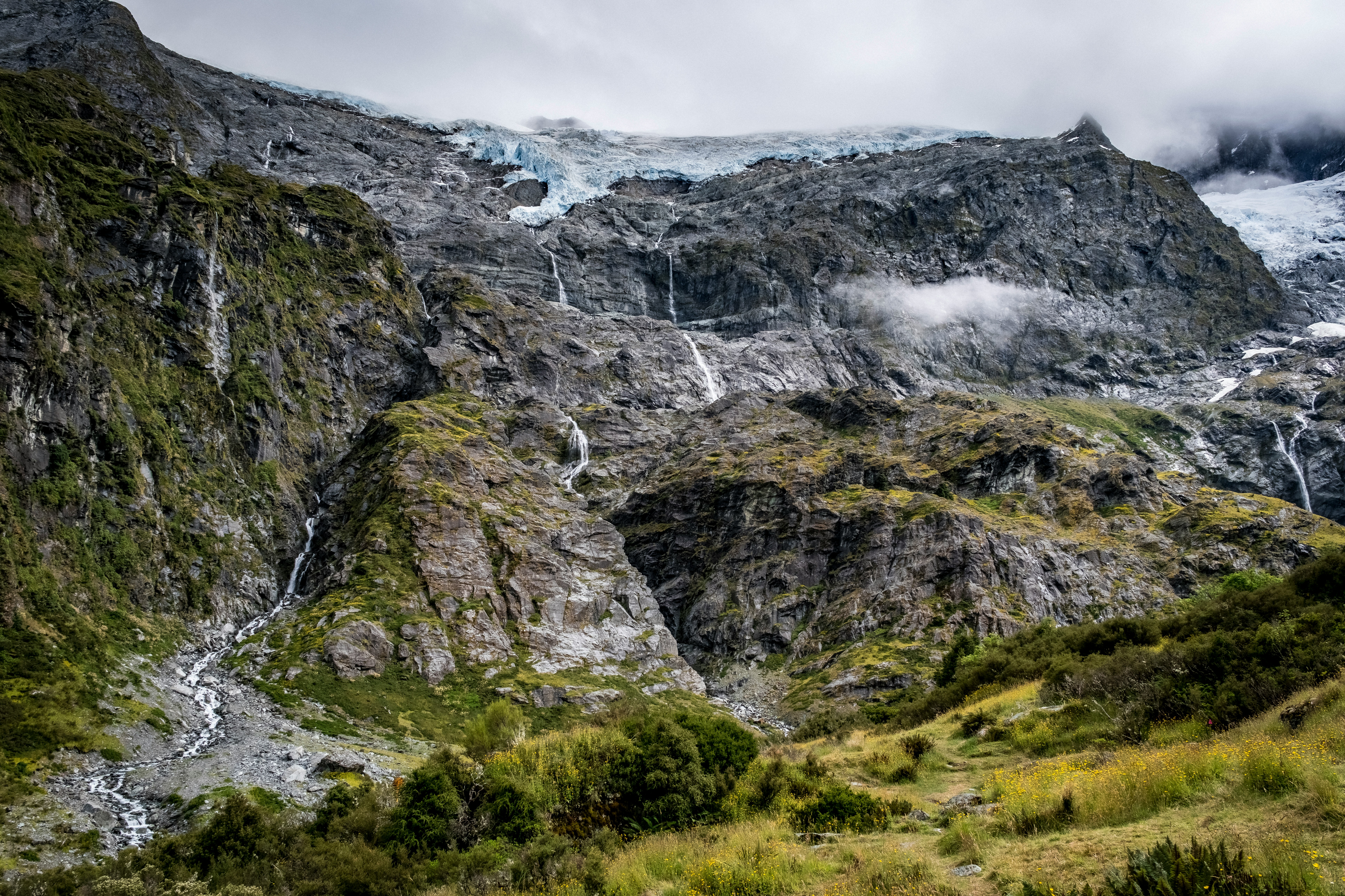 sign for rob roy glacier track, new zealand. glacier with small waterfalls coming down from it.